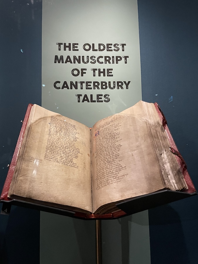 The Hengwrt Chaucer, a large vellum book bound in red leather from c.1400, open to the Prologue. It is on display in front of text which reads “the oldest manuscript of the Canterbury Tales”